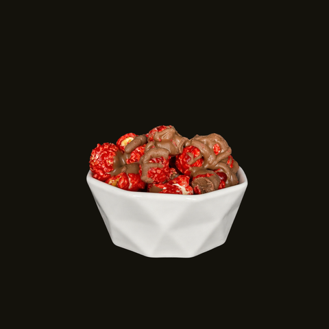White bowl filled with red cinnamon candied popcorn drizzled with chocolate  on a black background