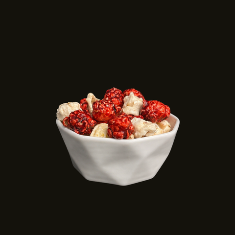 White bowl filled with red raspberry candied popcorn and white cheesecake candied popcorn on a black background