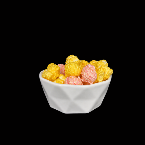 White bowl filled with pink raspberry and yellow lemonade popcorn on a black background